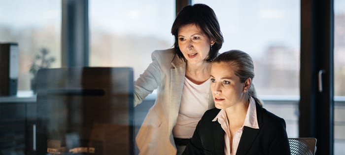 Businesswoman working late in front of a laptop and monitor in a modern office space.