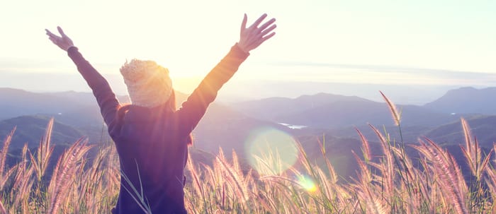 Happy Woman Enjoying Nature on grass meadow on top of mountain cliff with sunrise.