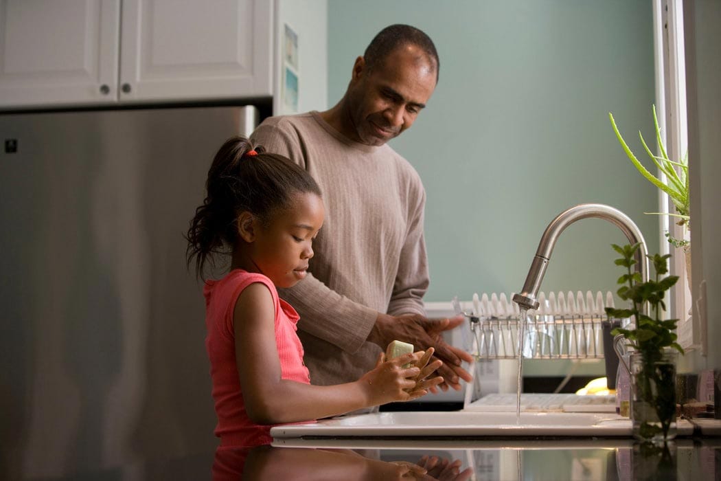 Father and daughter wash dishes together in the kitchen.