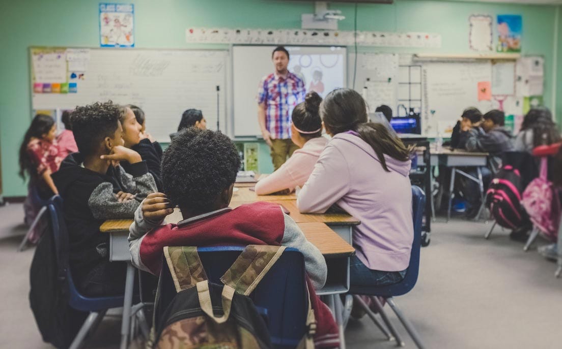 A fourth grade teacher welcomes his students to class after a long recess break.