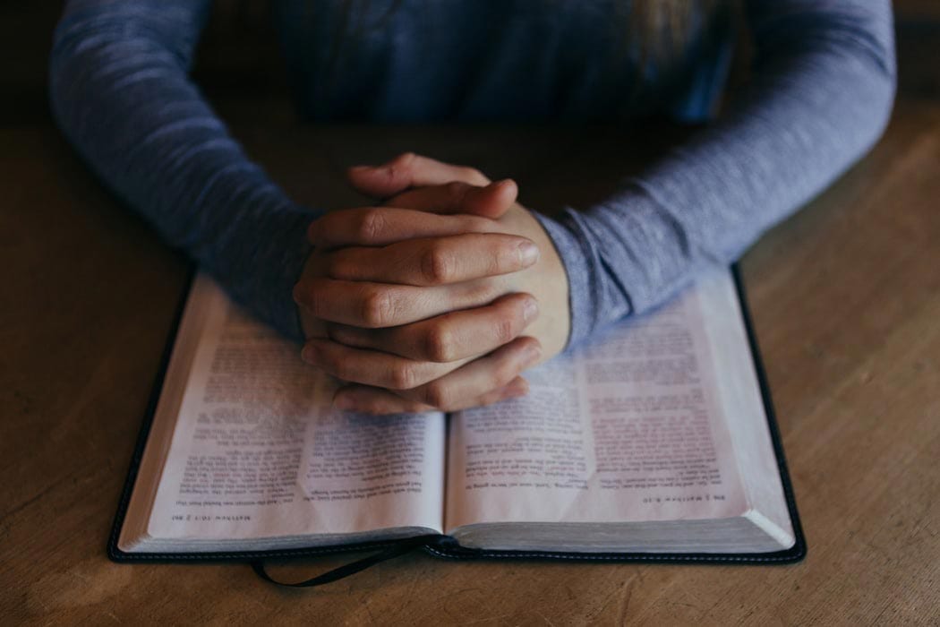 hands folded over a bible in prayer